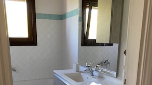 A bathroom with a white sink, a mirror, and a bathtub. - Apartment in village, green and relax (Stintino)