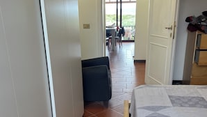 A hotel room with a bed, a chair, a wardrobe, and a view of the outdoor patio area. - Apartment in village, green and relax (Stintino)