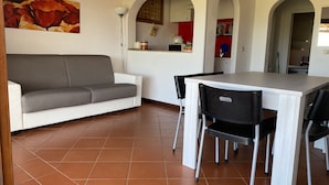 A modern kitchen with a dining area, featuring a white sofa, a dining table with chairs, and a tiled floor. - Apartment in village, green and relax (Stintino)