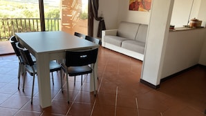A dining area with a table and chairs, a sofa, and a view of the outdoors. - Apartment in village, green and relax (Stintino)