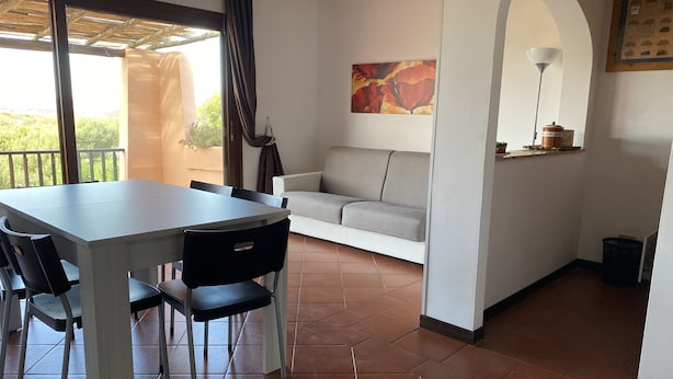 A dining area with a table and chairs, a sofa, a painting, and a lamp. - Apartment in village, green and relax (Stintino)