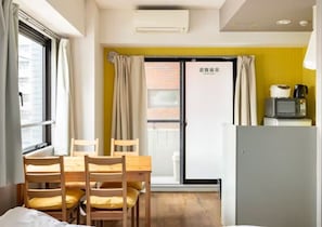 Une pièce avec une table et des chaises en bois, une petite kitchenette équipée d’un four à micro-ondes et une porte coulissante donnant sur un balcon.