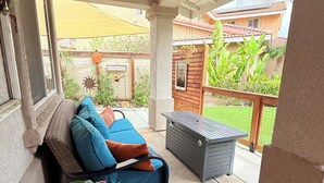 A covered balcony with a cushioned seating area, a potted plant, and a small table.
