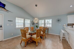 A dining area with wicker chairs and a glass-top table, a kitchen with white cabinets, and a ceiling fan.