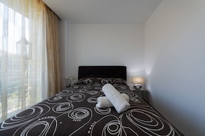 Une chambre d’hôtel avec un lit, une table de chevet, une lampe et une vue sur la ville par la fenêtre.