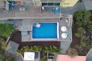 Vue aérienne d’un espace piscine comprenant des chaises longues, un jacuzzi et une petite piscine gonflable.