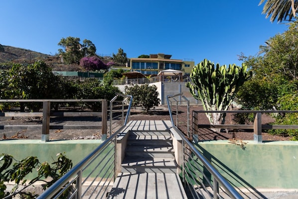 Un chemin menant à un bâtiment doté d’un escalier, entouré de verdure et de cactus.