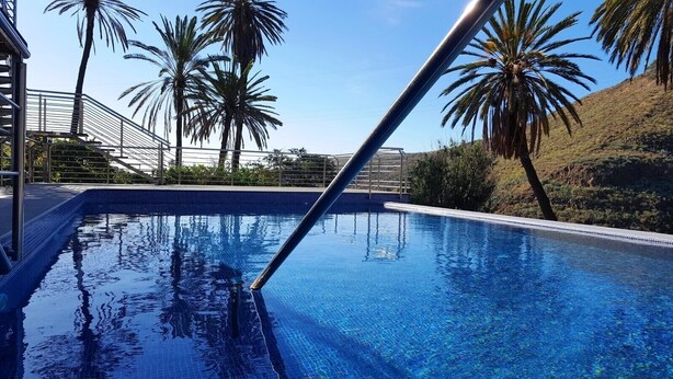A swimming pool with clear blue water, surrounded by palm trees and a metal railing. - VILLA OASIS - APART N - 5 (TELDE)