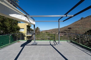 Un espace extérieur abrité, doté d’une structure en métal, d’une clôture verte et offrant une vue sur un paysage vallonné.
