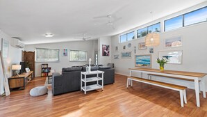 Ein geräumiges Wohnzimmer mit Holzboden, einem grauen Sofa, einem weißen Couchtisch und einer Holzbank.