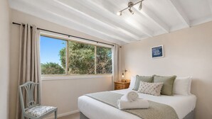 Ein Schlafzimmer mit Bett, Sessel, Nachttisch, Lampe und einem Fenster mit Vorhängen.