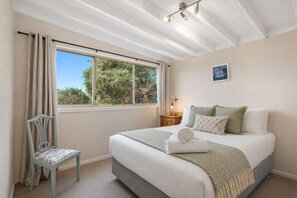 A bedroom with a bed, a chair, a nightstand, a lamp, and a window with curtains. - Bungalow at Bridgewater Bay by Ready Set Stay - Free WiFi and Family Friendly (Blairgowrie)