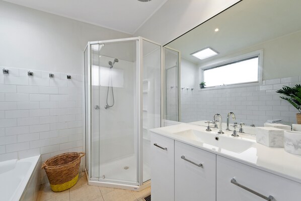 A modern bathroom with a glass-enclosed shower, white tiled walls, a large mirror, and a white sink with multiple faucets.