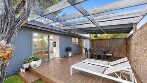 Eine überdachte Terrasse mit Holzdeck, Sitzgelegenheiten im Freien und Grillplatz.
