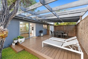 A covered patio with a wooden deck, outdoor seating, and a grill area. - Bungalow at Bridgewater Bay by Ready Set Stay - Free WiFi and Family Friendly (Blairgowrie)