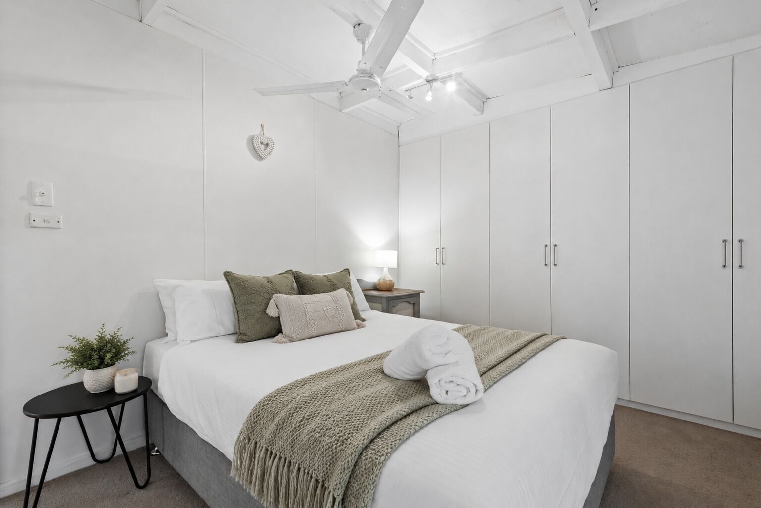 Ein Schlafzimmer mit einem Bett, einem Nachttisch mit Pflanze, einem Deckenventilator und weißen Schränken.