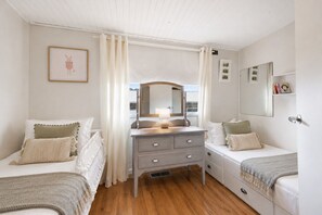 Ein Schlafzimmer mit zwei Einzelbetten, einem Schminktisch, einem Spiegel und einem Fenster mit Vorhängen.
