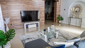 Una sala de estar moderna con un televisor de pantalla plana, una mesa de centro de vidrio, un sofá y una cocina al fondo.