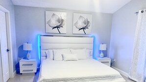 Un dormitorio moderno con una cama grande, dos mesitas de noche, un cabecero blanco y dos cuadros de rosas colgados en la pared.