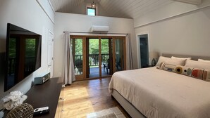 A bedroom with a large bed, a TV, a ceiling fan, and a sliding glass door leading to a balcony. - Sunapee Barn Retreat (Sunapee)