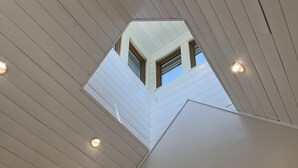 A modern interior with a sloped ceiling, recessed lighting, a door, and a mounted TV. - Sunapee Barn Retreat (Sunapee)