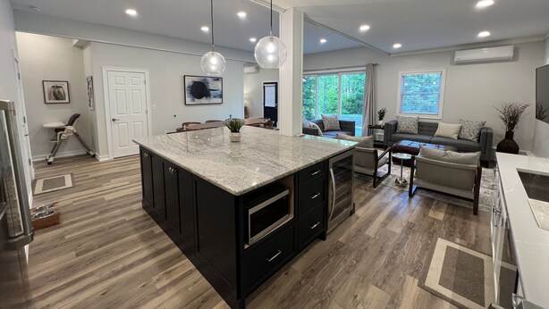 A modern kitchen with a large island, dark cabinetry, and a dining area with a sofa and coffee table. - Sunapee Barn Retreat (Sunapee)
