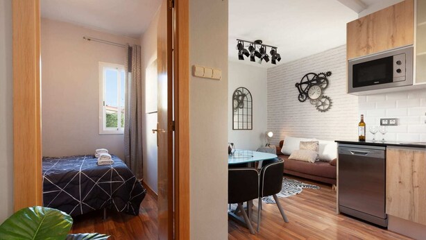 Ein kleines Zimmer mit Bett, Esstisch, Sofa und Küchenzeile inklusive Mikrowelle und Geschirrspüler.