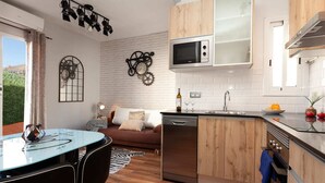 Eine moderne Küche mit Geschirrspüler, Mikrowelle und Holzschränken. Es gibt eine Essecke mit einem Glastisch und Stühlen sowie eine Couch mit Kissen.