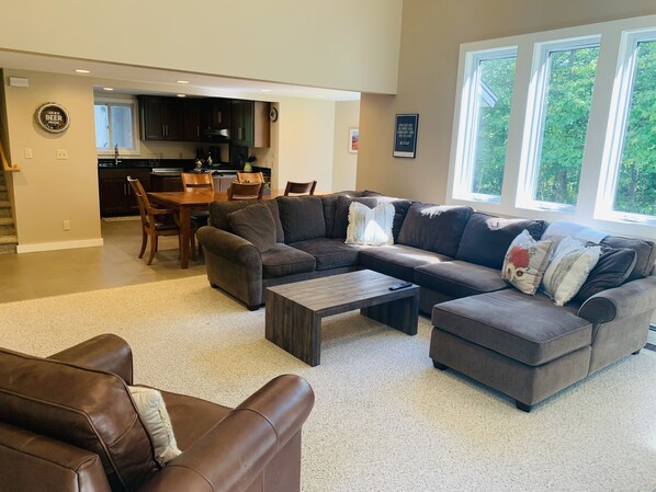 A spacious living room with a sectional sofa, a coffee table, and a dining area with a wooden table and chairs.