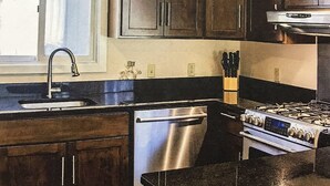 A kitchen with dark wooden cabinets, stainless steel appliances, and a black granite countertop.