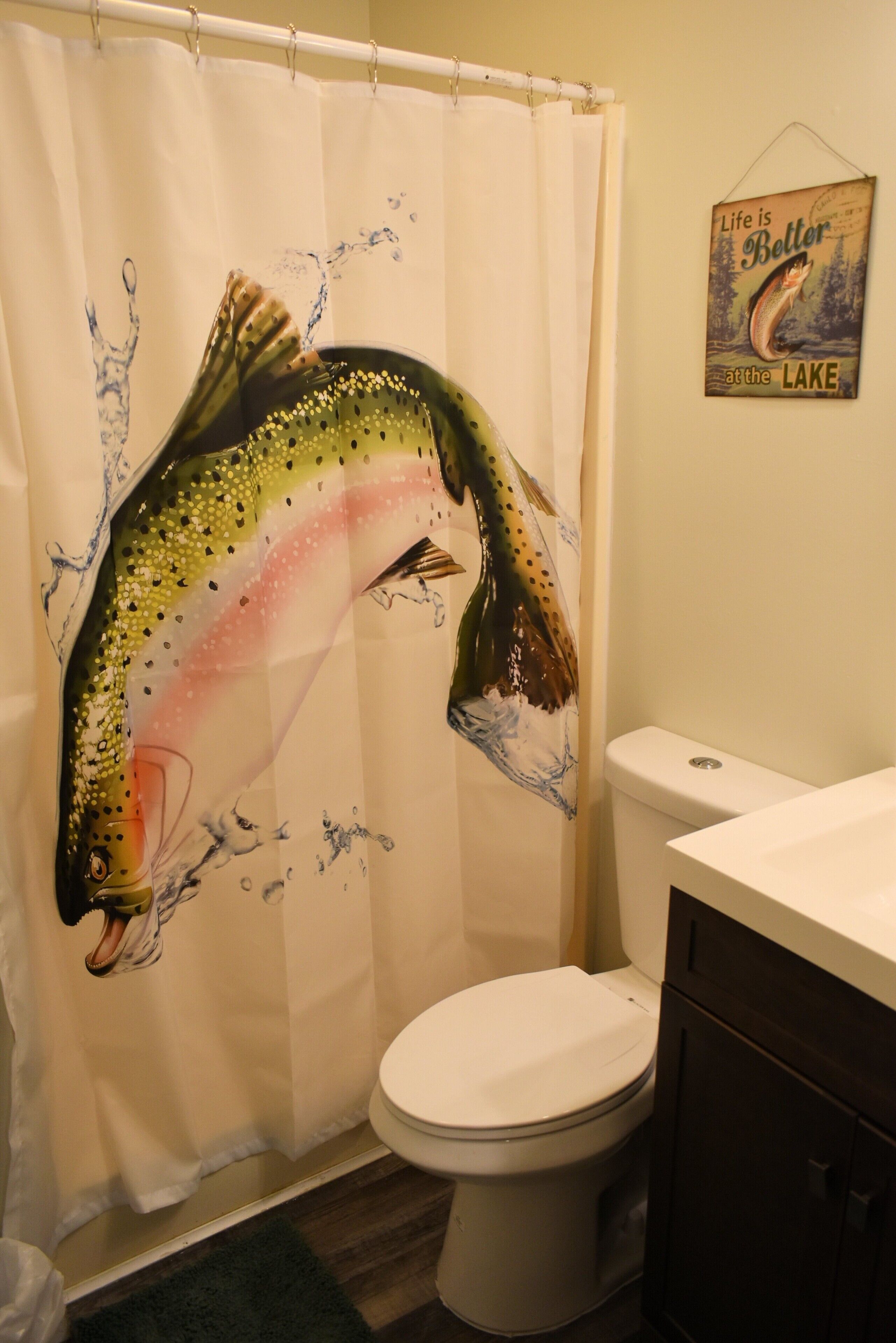 A bathroom with a shower curtain depicting a fish, a toilet, and a cabinet.