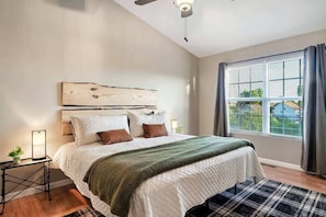 A bedroom with a bed, a nightstand, a lamp, a window with curtains, and a ceiling fan.