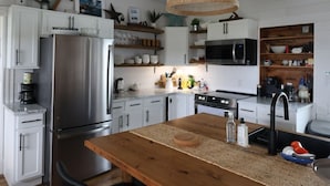 Una cocina moderna con armarios blancos, una isla de madera, sillas negras y una lámpara colgante de tejido.
