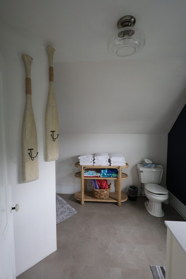 A bathroom with a toilet, a sink, a shower area, and a towel rack with folded towels.