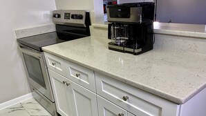 Une cuisine avec des meubles blancs, un sol carrelé en marbre, une machine à café et une cuisinière.