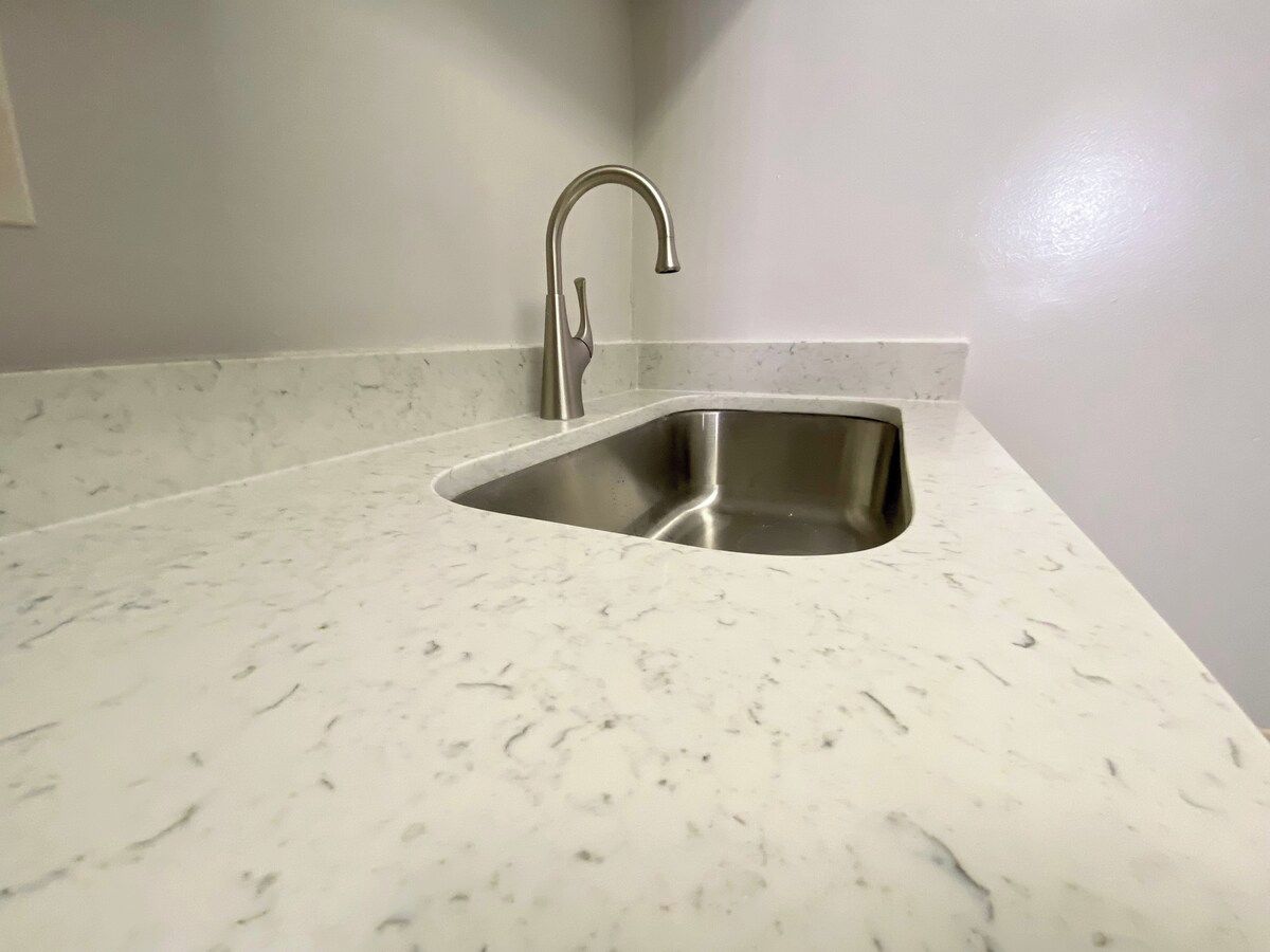 A kitchen with a stainless steel sink and a marble countertop.