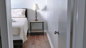 A bedroom with a bed, bedside table, lamp, and wooden flooring.