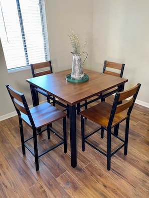 Mesa de jantar com quatro cadeiras, um jarro decorativo e uma janela com persianas.