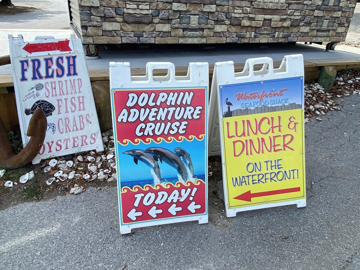 Three promotional signs advertising a dolphin adventure cruise, fresh seafood, and a lunch and dinner on the waterfront.