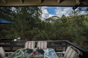 An outdoor patio with a table and chairs, overlooking a forested area with mountains in the background. - Beautiful Mtn Views, Hot Tub, short walk to Cafe Aroma (monthly rental) (Idyllwild-Pine Cove)