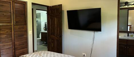 Een slaapkamer met een bed, een aan de muur bevestigde televisie, houten kasten en een badkamer zichtbaar door een geopende deur.