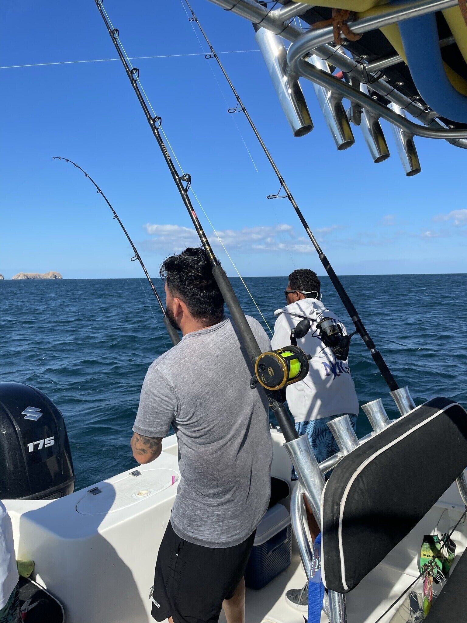 A boat with two people fishing, a clear blue sky, and calm sea.