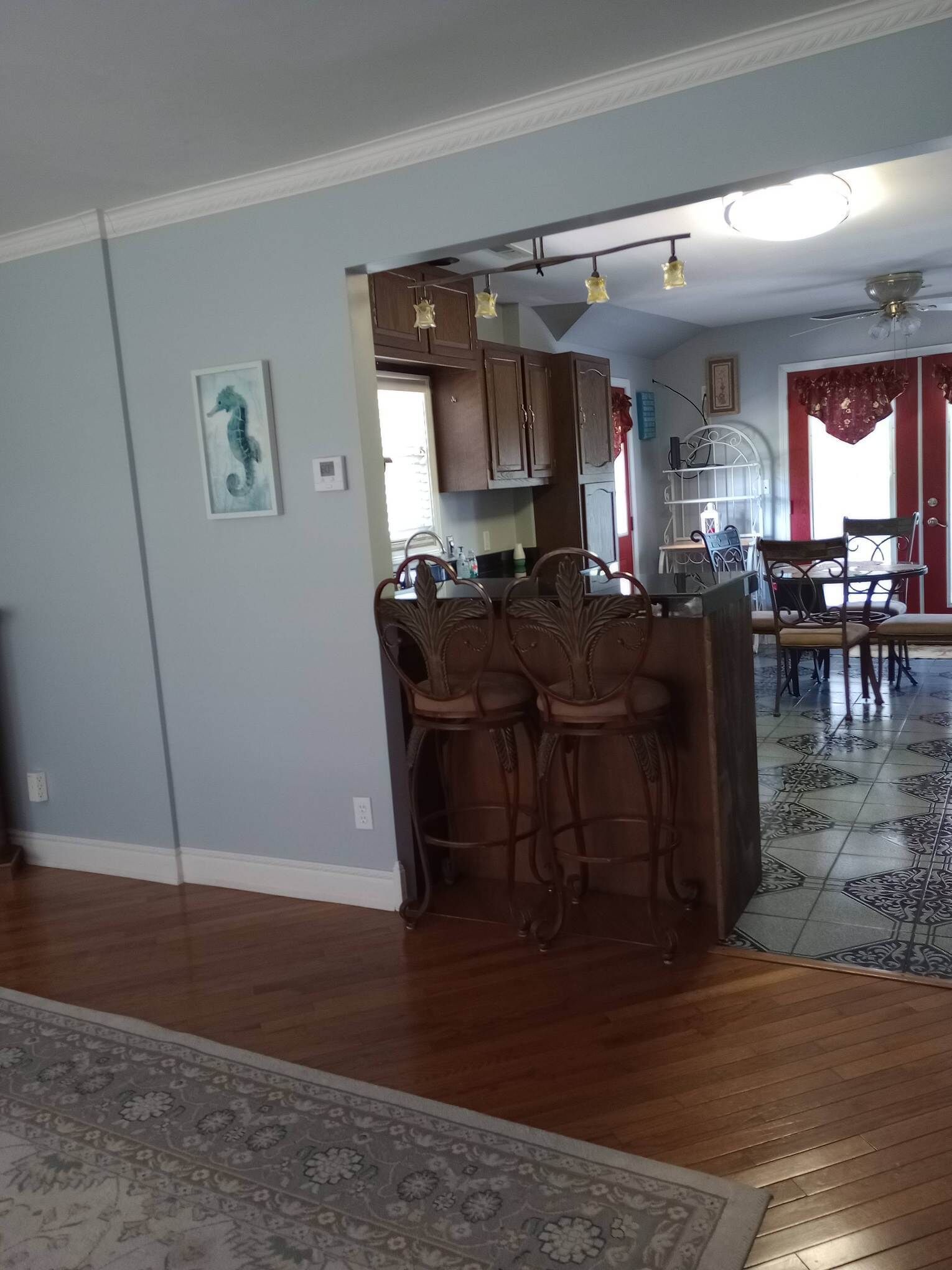 A spacious living area with a wooden floor, a dining table with chairs, and a kitchen area with cabinets and a hanging light fixture.