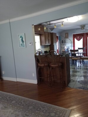 A spacious living area with a wooden floor, a dining table with chairs, and a kitchen area with cabinets and a hanging light fixture.
