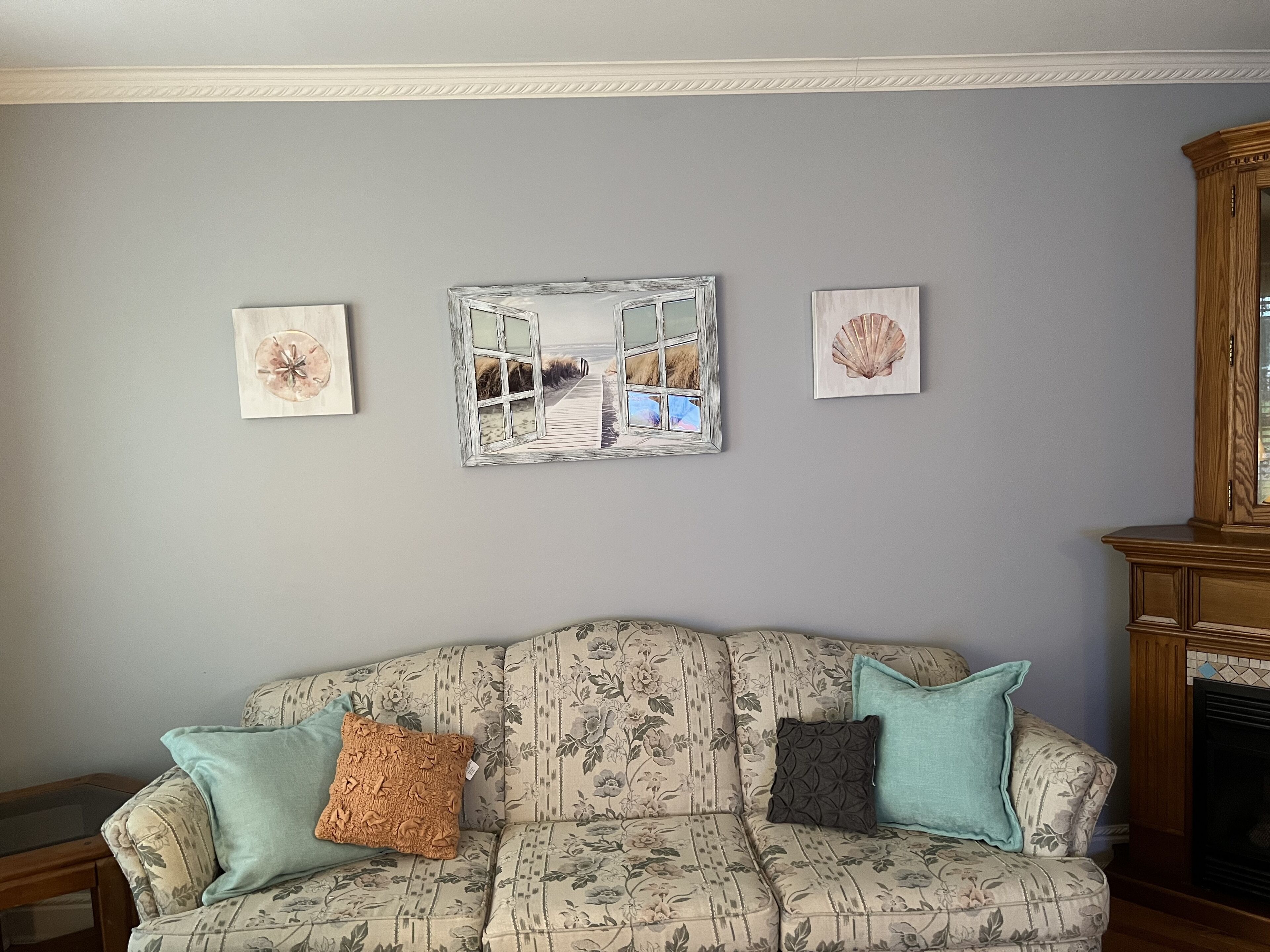 A living room with a floral-patterned sofa, three wall-mounted artworks, and a wooden cabinet.