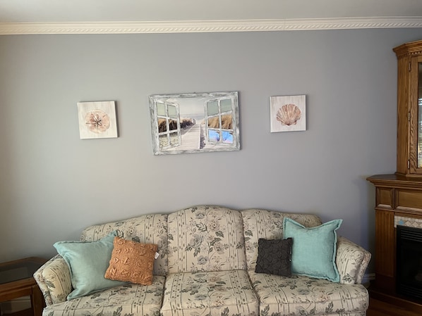 A living room with a floral-patterned sofa, three wall-mounted artworks, and a wooden cabinet.