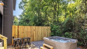 Een hottub met houten treden, een houten omheining en een zitgedeelte met stoelen.