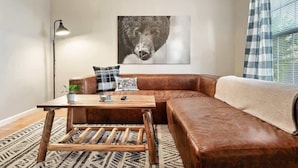 Een woonkamer met een bruine leren bank, een houten salontafel en een groot kunstwerk van een beer aan de muur.