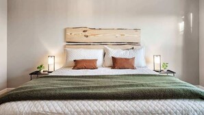 Een opgemaakt bed met een groene deken, twee nachtkastjes met lampen, en een houten hoofdbord.