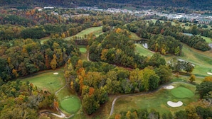 Luchtbeeld van een golfbaan, omringd door herfstkleuren en een klein stadje op de achtergrond.